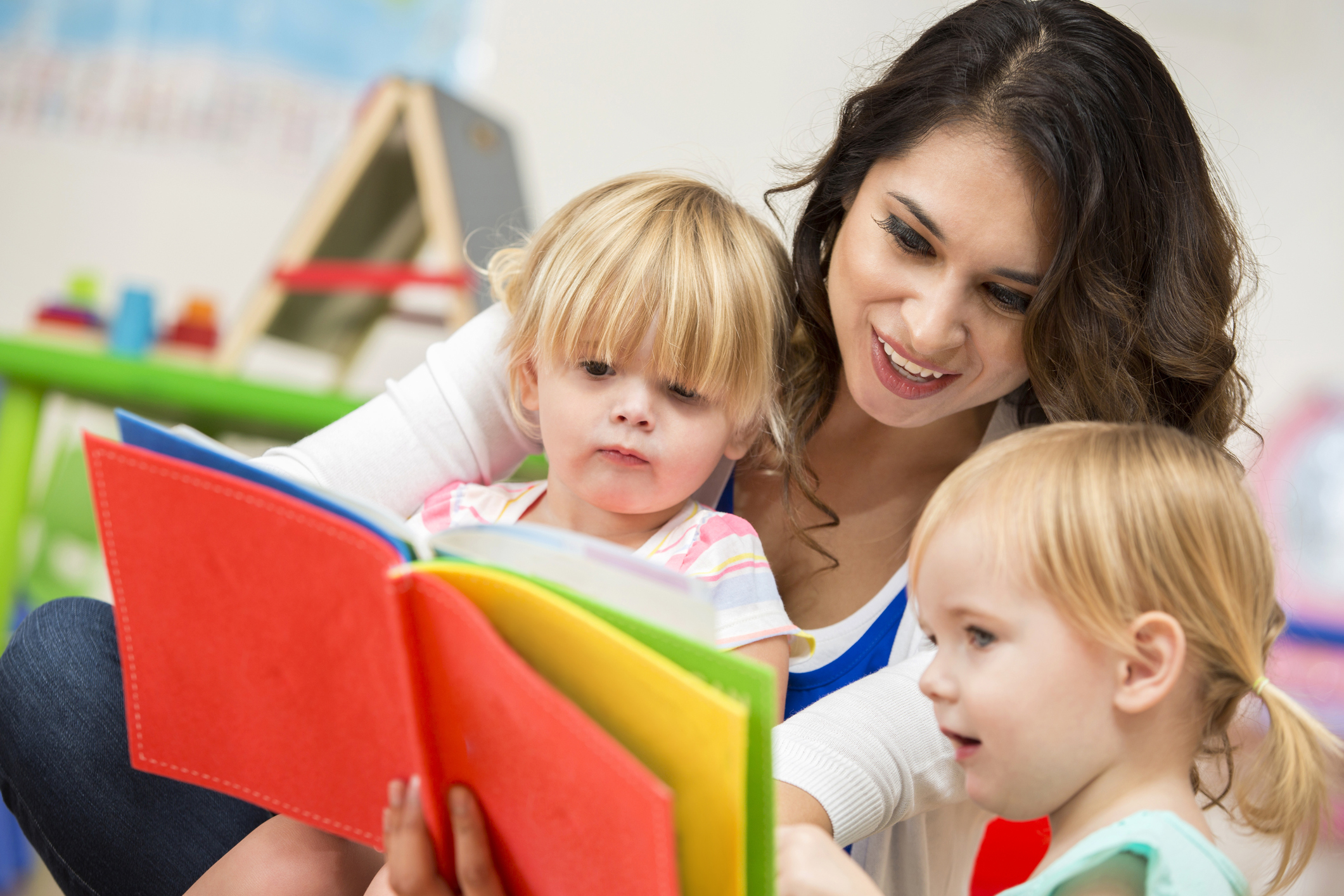 Young adult female teacher reading a book to two preschoolers
